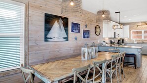 A kitchen with wooden walls, a dining table with chairs, and pendant lights. - Lagoon Views | Beach Access | Pool and Pier Amenities (Gulf Shores)