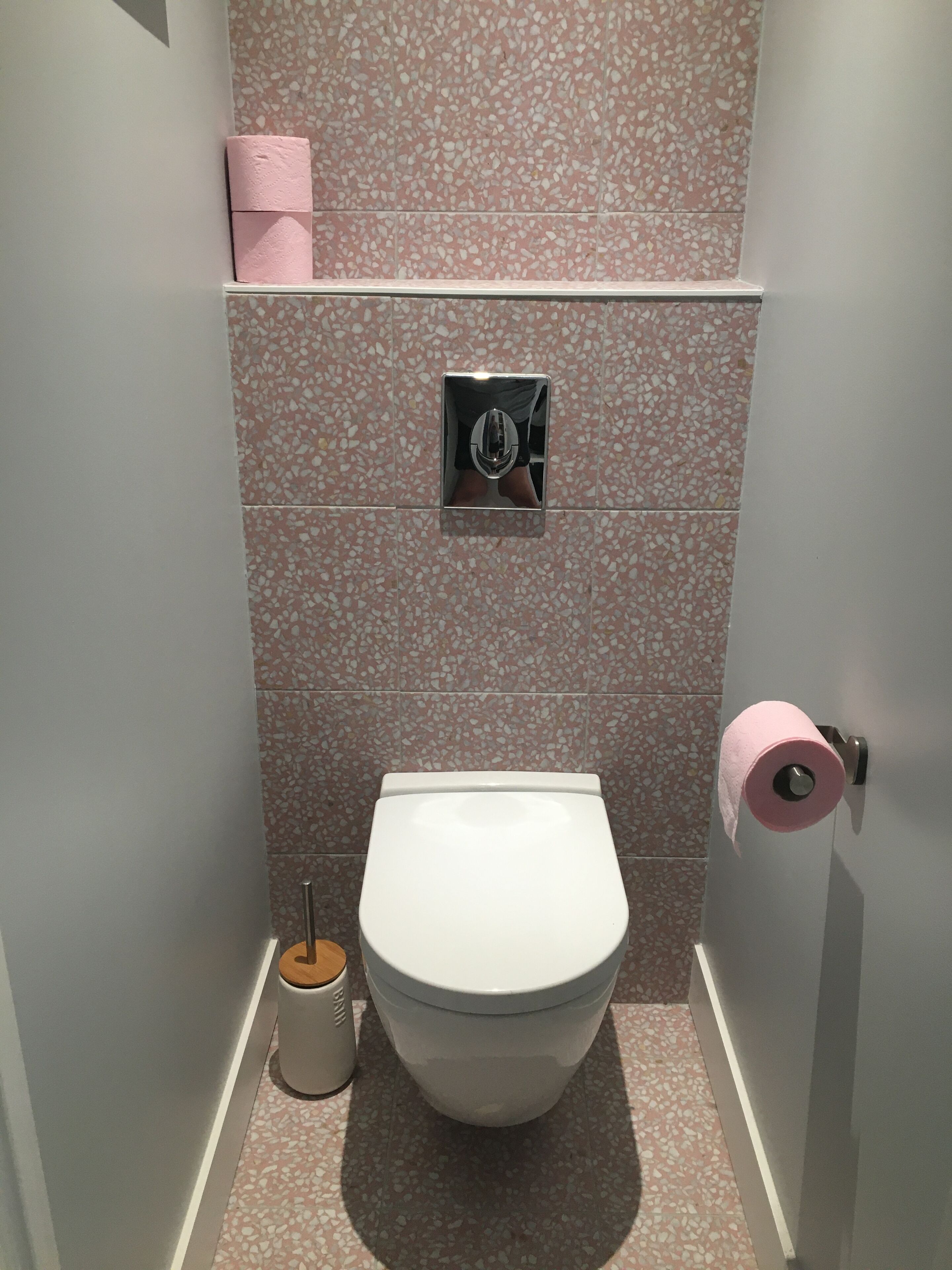 Un baño con inodoro blanco, dispensador de papel higiénico rosa y un cubo de basura.