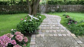A stone pathway leading through a garden with various flowering plants and a wooden fence in the background. - Urlaub in der Zauberhaft Renovierten Krümelkate (Witzwort)