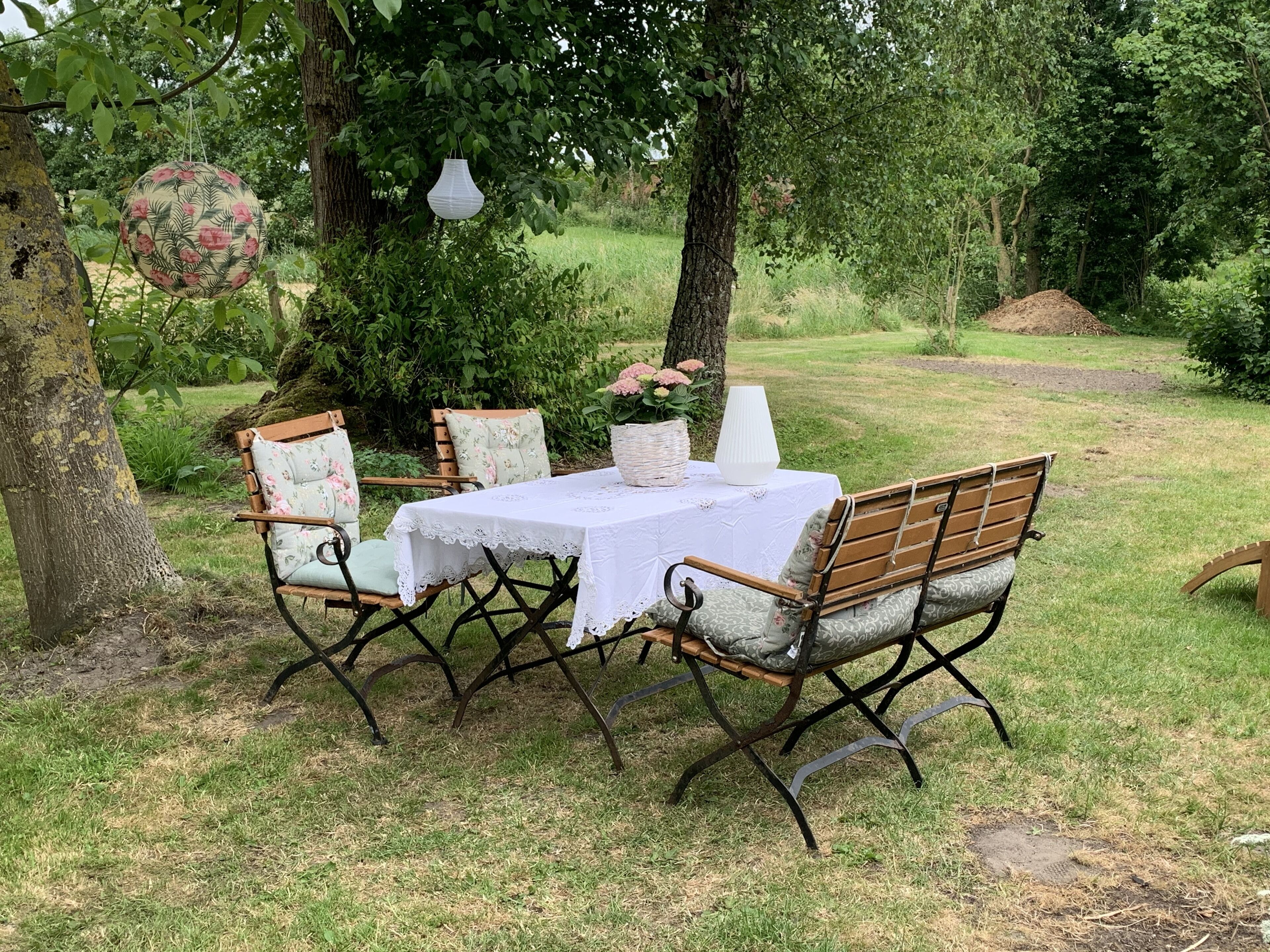 An outdoor seating area with a table and chairs, surrounded by trees and greenery.