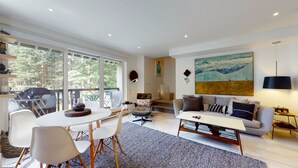 A modern living room with a large window, a sofa, a coffee table, and a bookshelf.