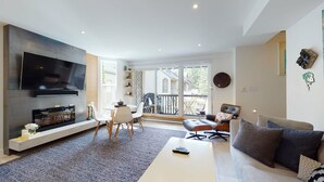 A modern living room with a flat-screen TV, a fireplace, a dining area, and a balcony with a view.