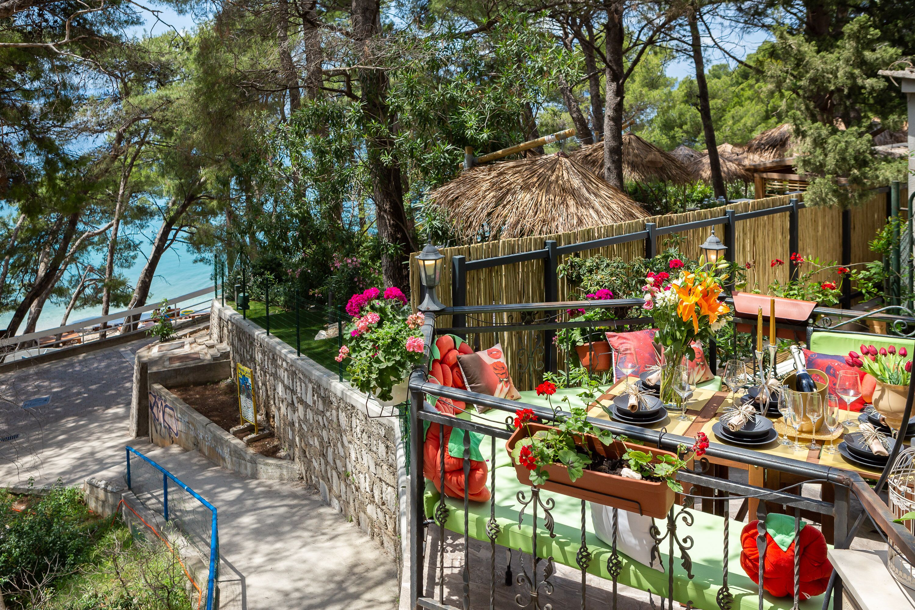An outdoor dining area with a table set for a meal, surrounded by potted plants and flowers.