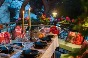 Un montaje para comer al aire libre con una mesa dispuesta para una comida, destacando platos negros, copas de vino y velas.