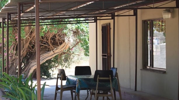 A covered outdoor seating area with a table and chairs, a tree, and a window. - Old farmhouse for 3 in Limpopo Province (Lephalale)