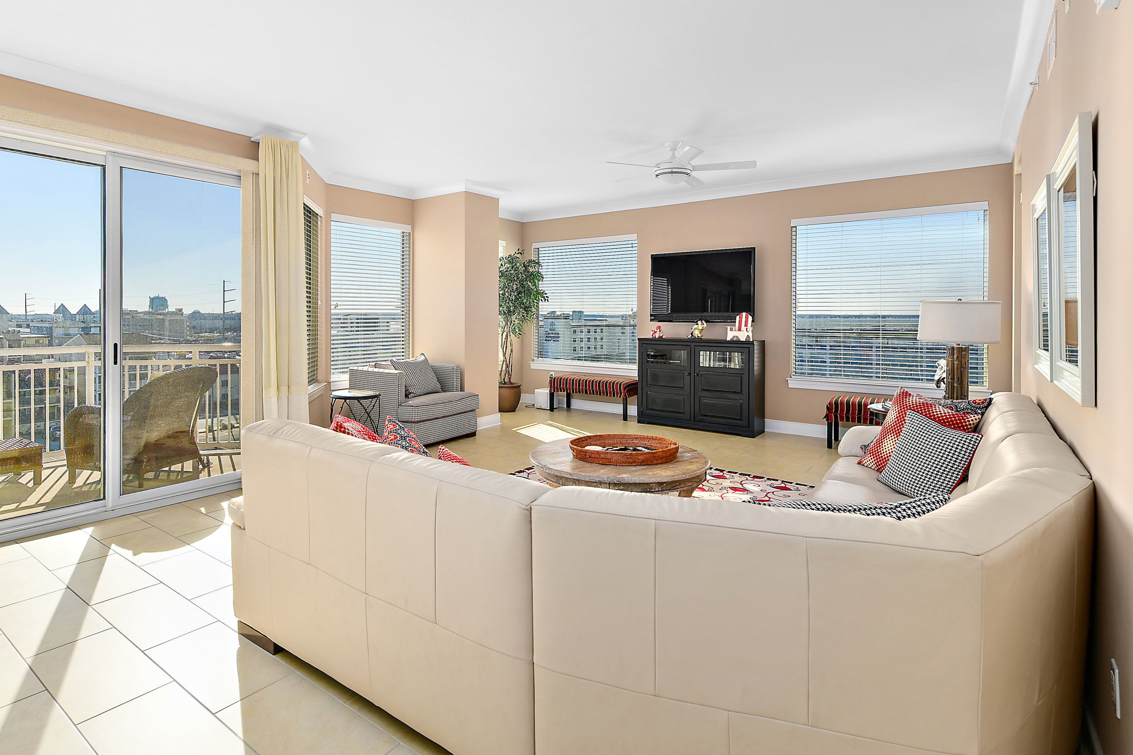 A spacious living room with a large sofa, a flat-screen TV, and a balcony with a city view.