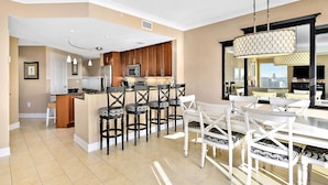 Una cocina moderna con armarios de madera, una isla central con taburetes y una zona de comedor con mesa y sillas blancas.
