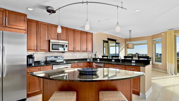 Una cocina moderna con armarios de madera, electrodomésticos de acero inoxidable, una isla central con taburetes y grandes ventanales con vistas a la ciudad.