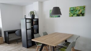 Un espace de salle à manger moderne avec une table en bois, des chaises grises, une bibliothèque noire et une suspension.