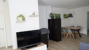 Un salon moderne doté d’un téléviseur à écran plat, d’un canapé, d’un coin repas avec une table et des chaises, et d’un meuble noir.