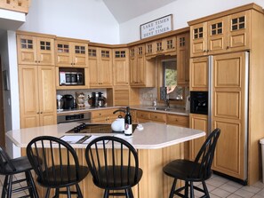 A kitchen with wooden cabinets, a stainless steel refrigerator, a large island with bar stools, and a sign that reads "LAKE TIMES are the BEST TIMES".
