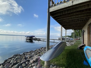 A lakeside view with a dock extending into calm water, a covered seating area, and a kayak on the shore.