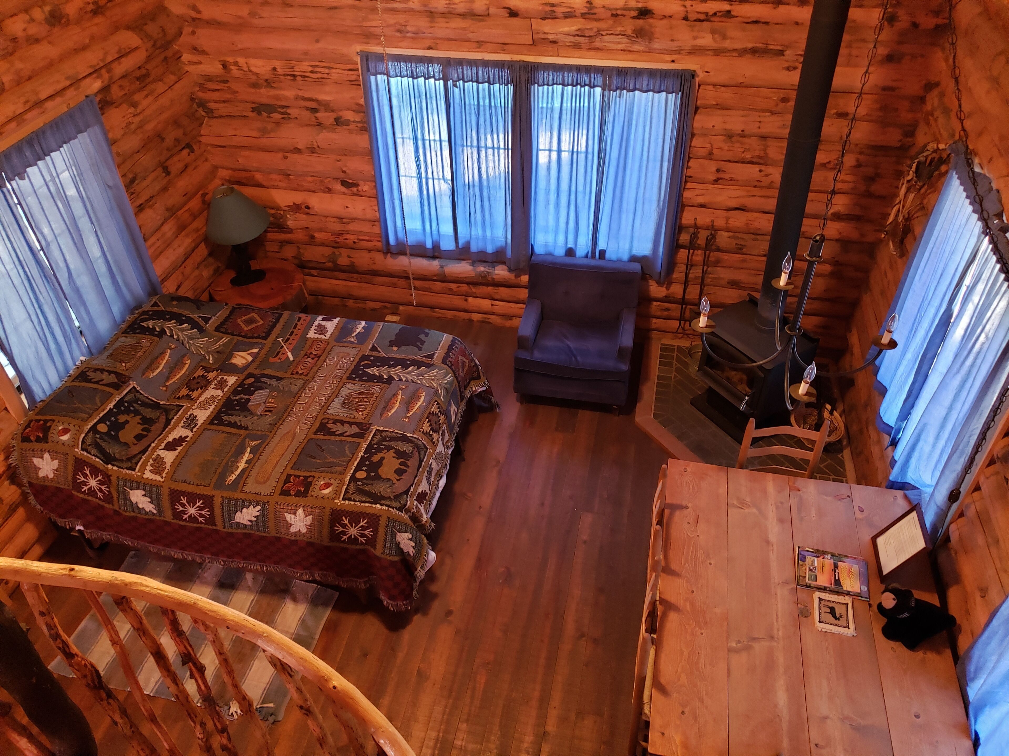 A log cabin room with a bed, a chair, a fireplace, and a window with curtains.