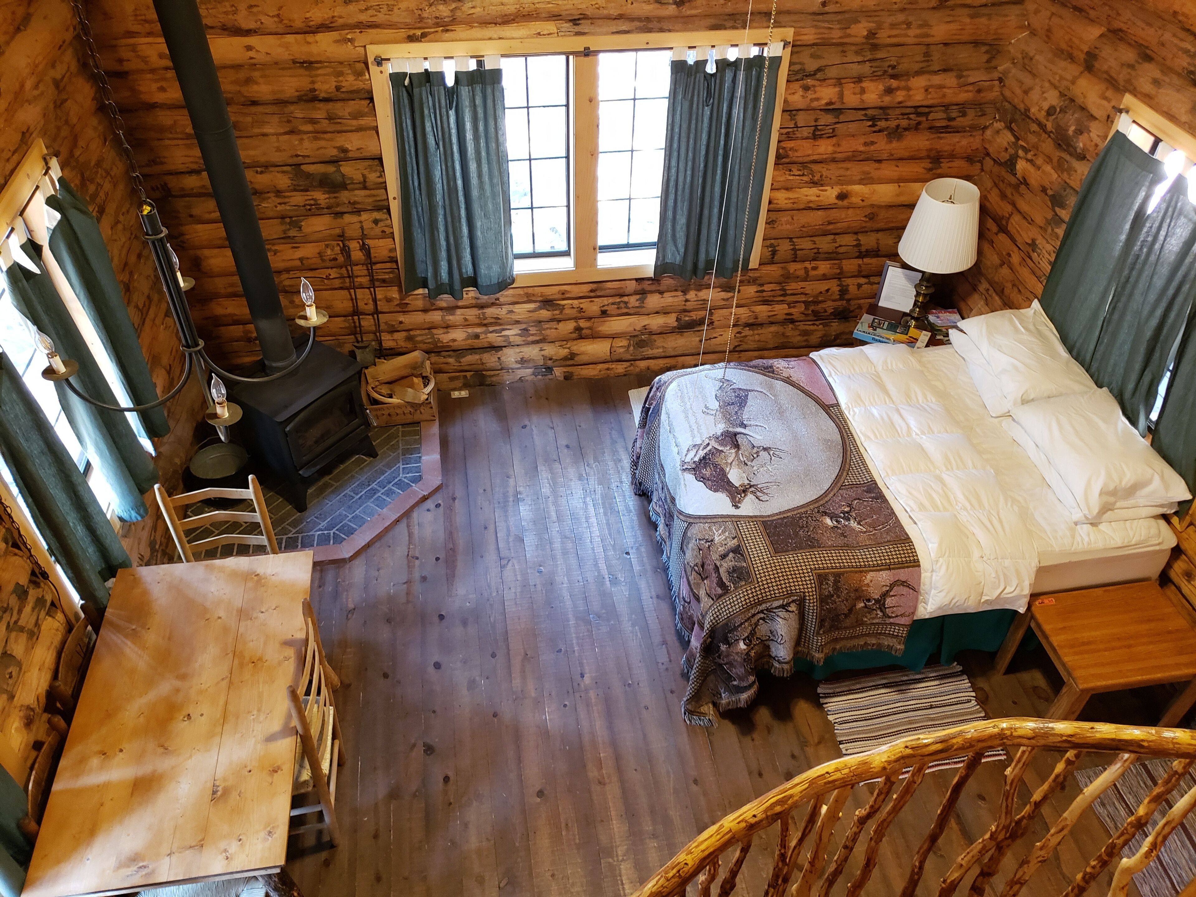 A cozy cabin-style room with a wooden interior, a bed with patterned bedding, a fireplace, and a window with curtains.