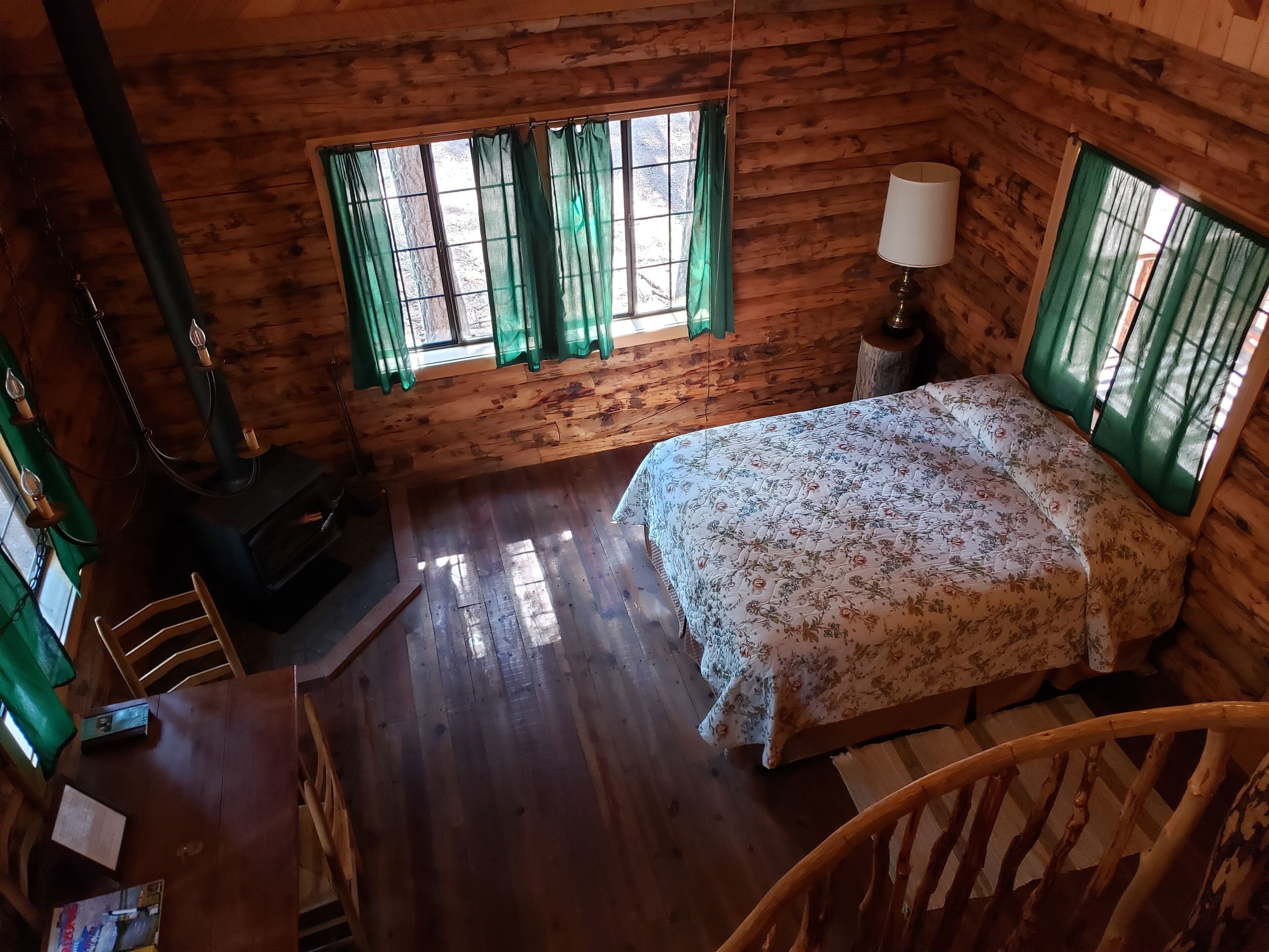 Camera da letto in una baita di legno con un letto, un tavolo, una lampada e un camino.