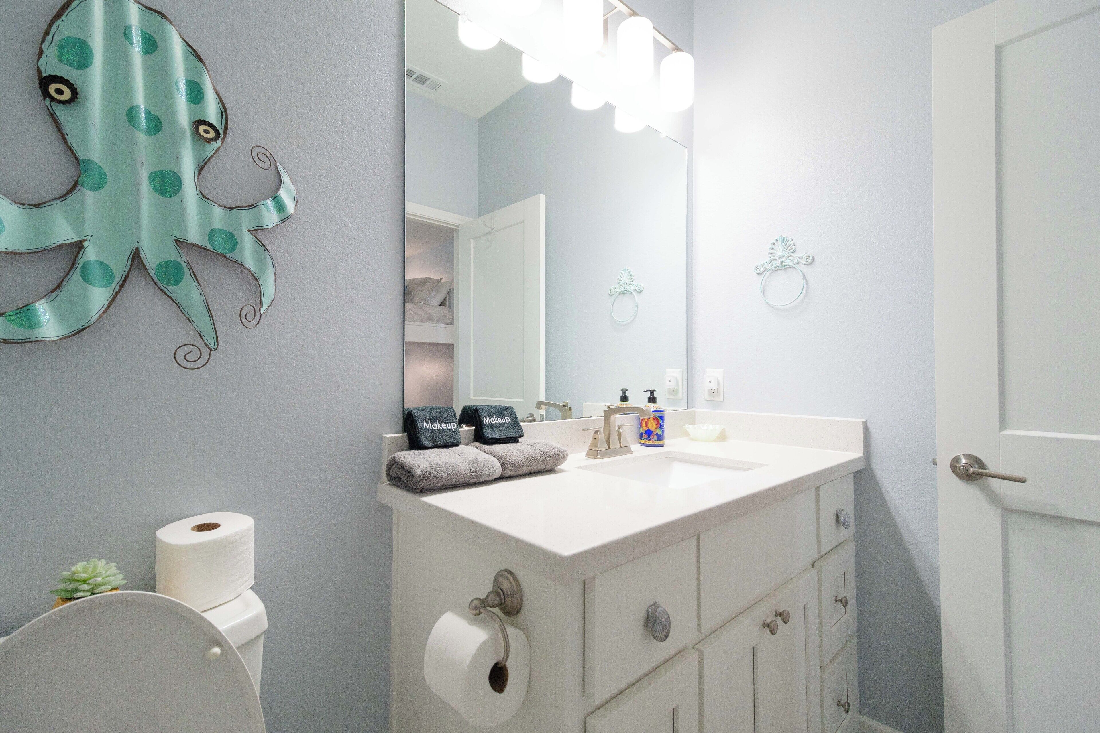 Ein Badezimmer mit Toilette, Waschbecken, einem beleuchteten Spiegel und einem dekorativen Oktopus an der Wand.
