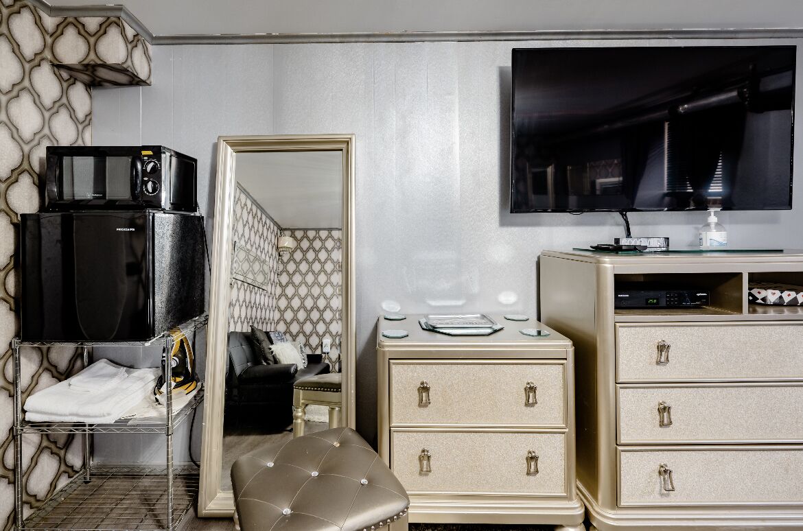 A hotel room with a kitchenette, a large mirror, a television, and a minibar.