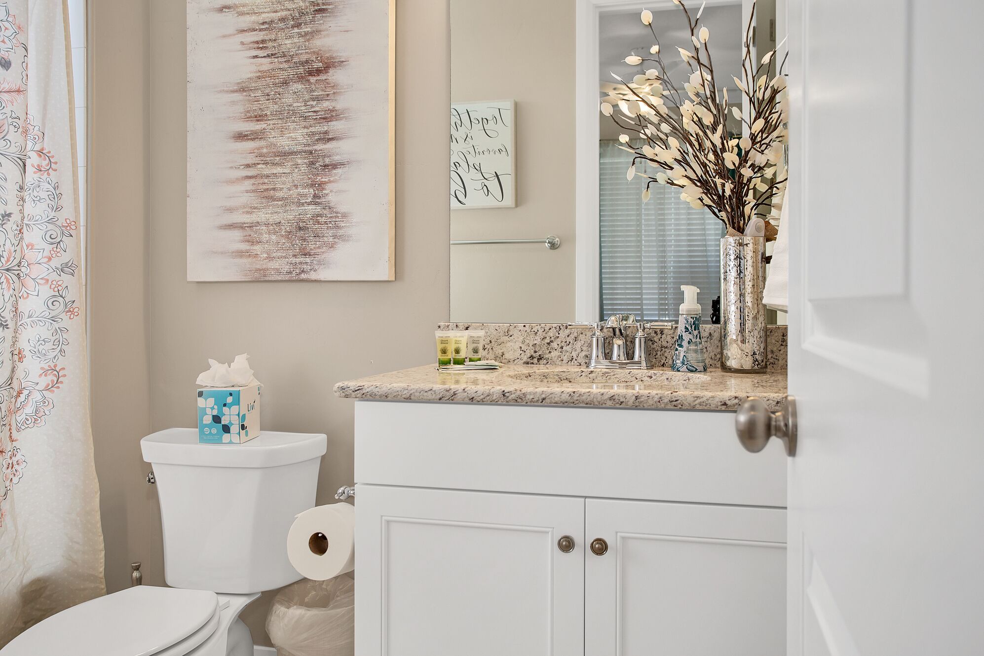 A bathroom with a toilet, a sink with a marble countertop, a mirror, and a decorative plant.