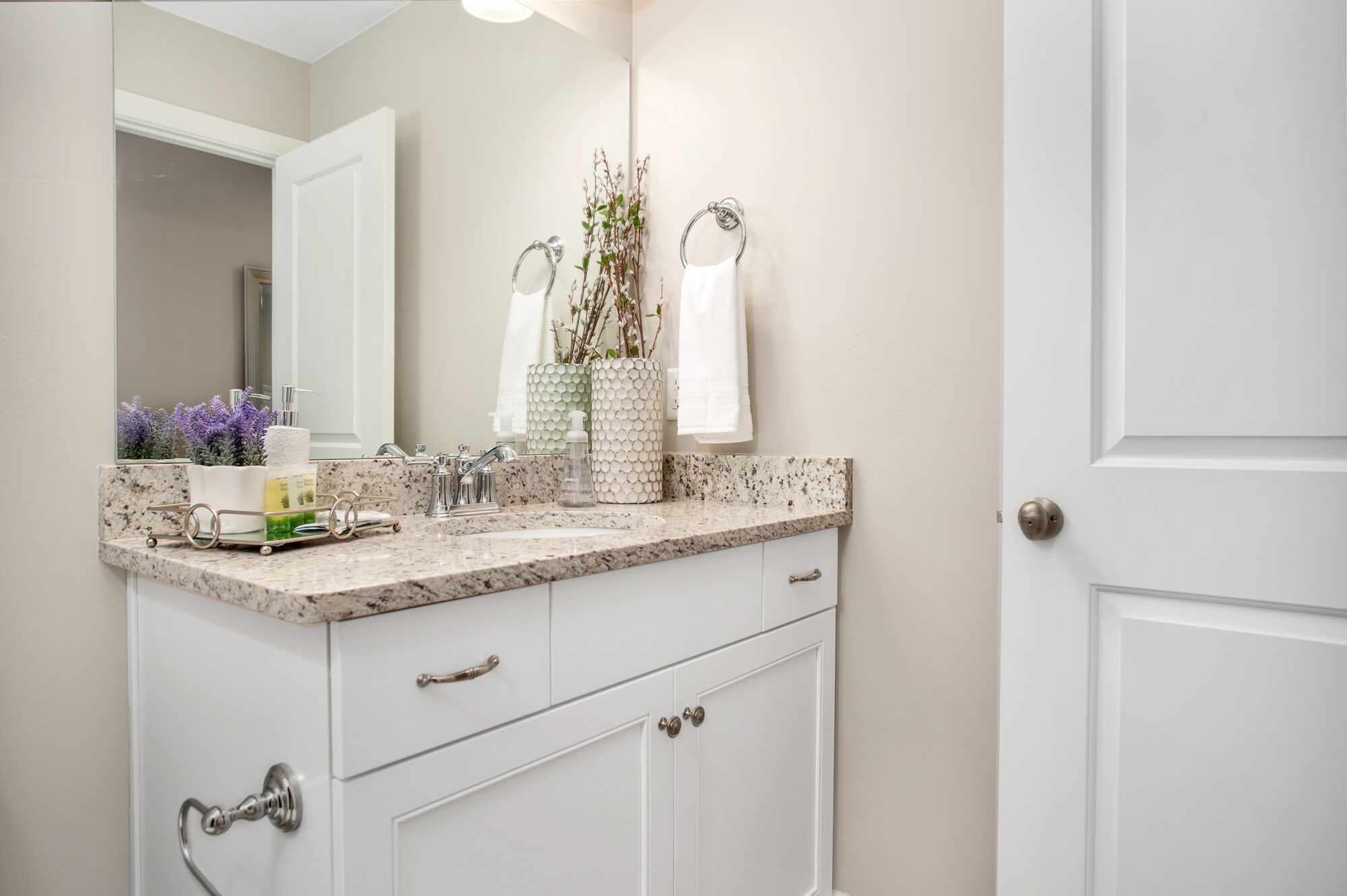 A bathroom with a white vanity, a mirror, a sink with a soap dispenser, and a towel rack.