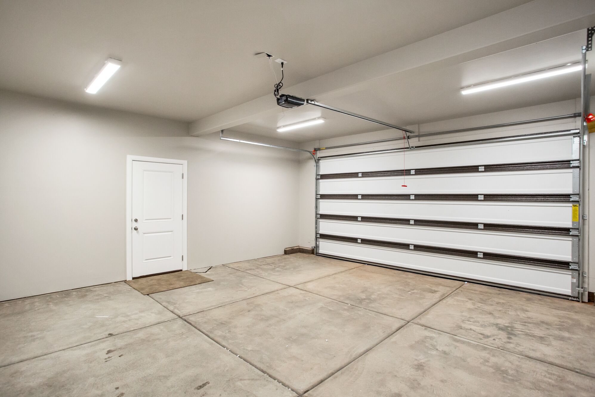 A clean, empty garage with a white door, a metal garage door, and fluorescent lighting.
