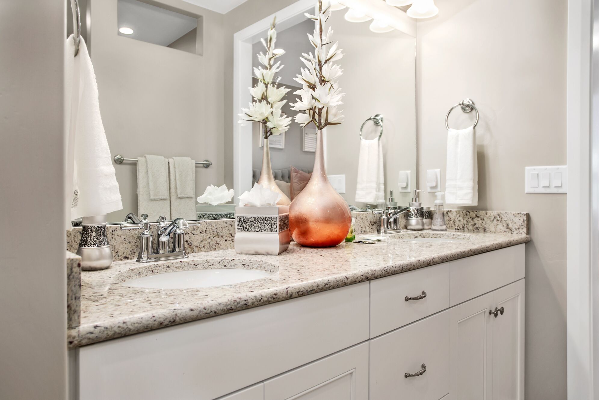 A bathroom with two sinks, a large mirror, and a vase with white flowers.