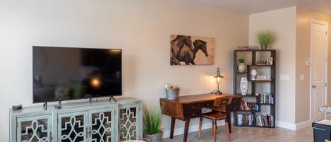 Una sala de estar con una televisión de pantalla plana, un escritorio de madera, una estantería y una zona de comedor.