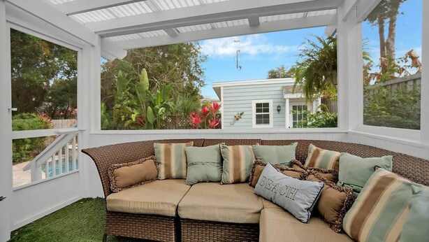 A covered outdoor seating area with a wicker sofa and cushions, a view of a house, and lush greenery. - Pool, Hot Tub, Walk to Ice Plant, Smart TVs, BBQ (St. Augustine)