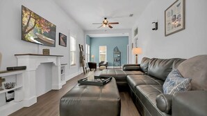 A living room with a sectional sofa, ottoman, fireplace, and artwork on the walls. - Pool, Hot Tub, Walk to Ice Plant, Smart TVs, BBQ (St. Augustine)