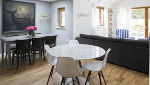Un coin repas avec une table ronde, des chaises et un vase de fleurs. Un grand tableau orne le mur, et une bibliothèque remplie de livres se trouve à proximité.