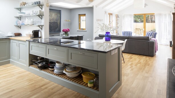 A modern kitchen with a central island, wooden flooring, and a dining area with a gray sofa and a window. - Camber Sands House
Luxury 5 En-Suite bedrooms, minutes from beach. Dog friendly! (Camber)
