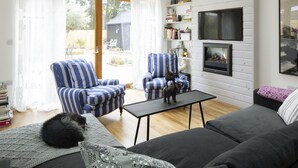 A cozy living room with a fireplace, striped armchairs, a sofa, and a cat on a blanket. - Camber Sands House
Luxury 5 En-Suite bedrooms, minutes from beach. Dog friendly! (Camber)