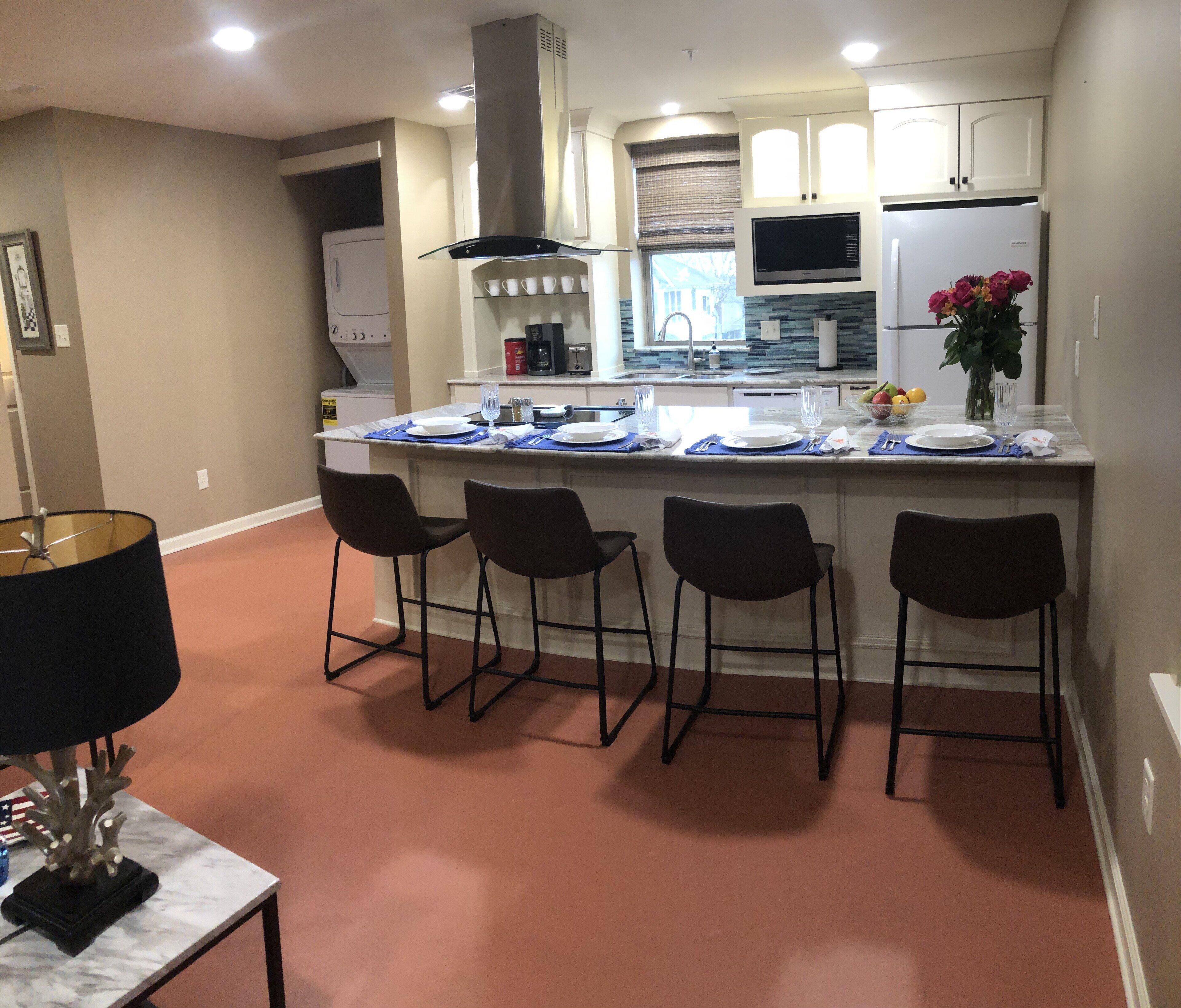 A modern kitchen with a central island, bar stools, and a dining area with a table and chairs.