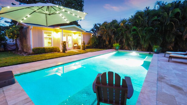 A swimming pool with a chair and umbrella, surrounded by a house and palm trees. - One-of-a-Kind Home! Pet Friendly, Fenced, Private Pool! 1 mi to Downtown & Beach (Venice)