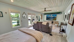 A bedroom with a bed, a seating area with a sofa and chairs, a ceiling fan, and a large window. - One-of-a-Kind Home! Pet Friendly, Fenced, Private Pool! 1 mi to Downtown & Beach (Venice)