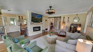 A spacious living room with a fireplace, a dining area, and a kitchen with wooden cabinets. - One-of-a-Kind Home! Pet Friendly, Fenced, Private Pool! 1 mi to Downtown & Beach (Venice)