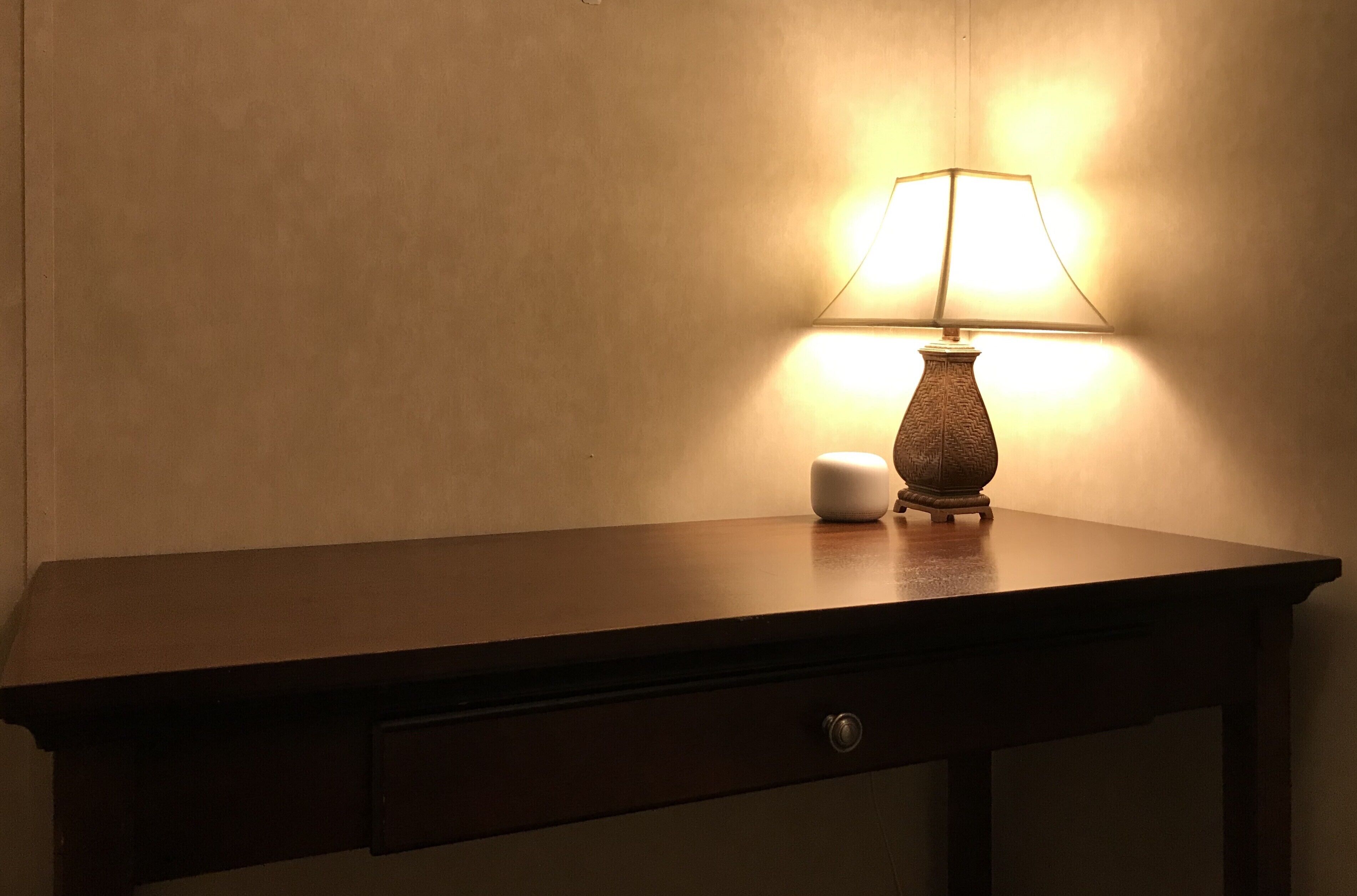 A wooden desk with a lamp and a small white object on it.