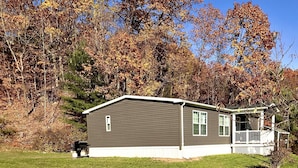 Einbungalow mit Veranda, umgeben von einem Rasen und Bäumen mit Herbstlaub.