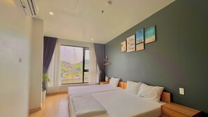 A modern hotel room with a large bed, a wooden nightstand, and a view of a mountainous landscape through the window. - Rustic House (Hai Phong)