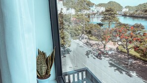 A view from a window overlooking a street with trees and buildings, a body of water, and a bridge in the distance. - Rustic House (Hai Phong)