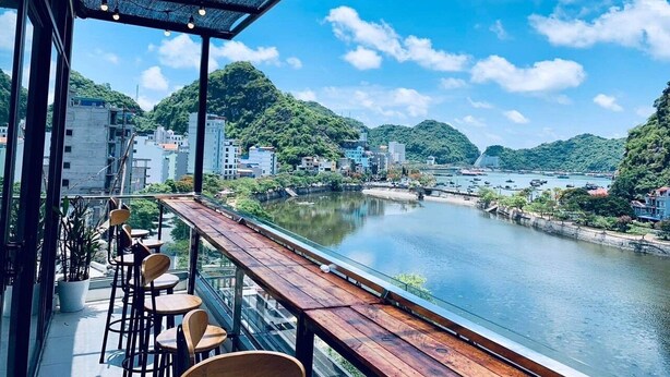 A terrace with a view of a river, wooden seating, and a metal railing. - Rustic House (Hai Phong)