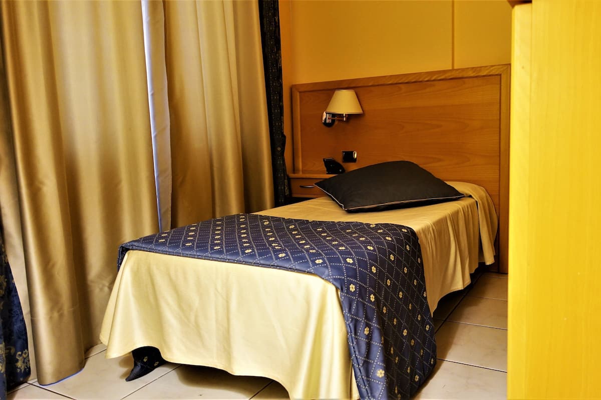 A hotel room with a bed, a nightstand, a lamp, and a wooden headboard.