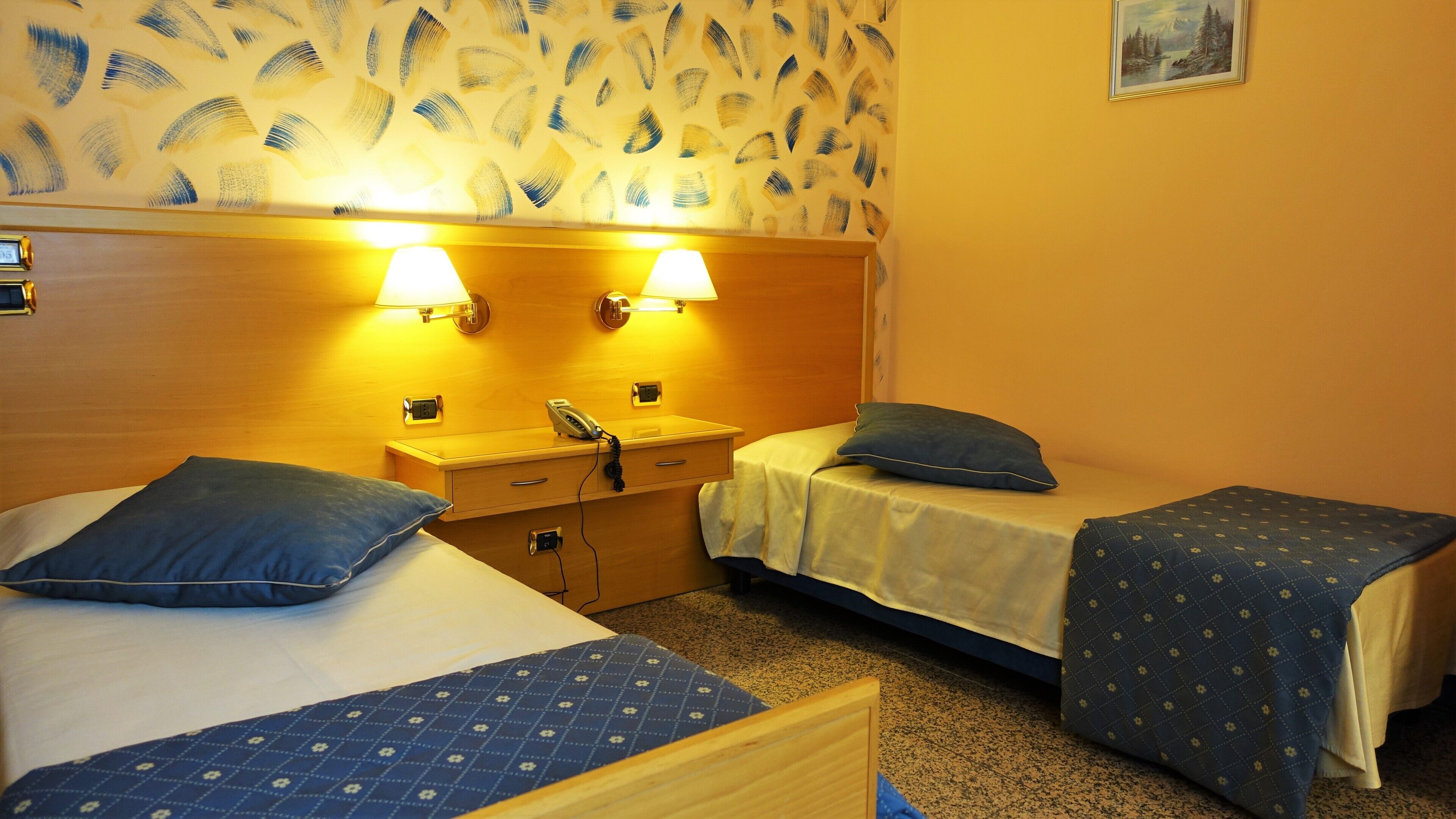 A hotel room with two beds, a wooden dresser, a nightstand with a lamp, and a painting on the wall.