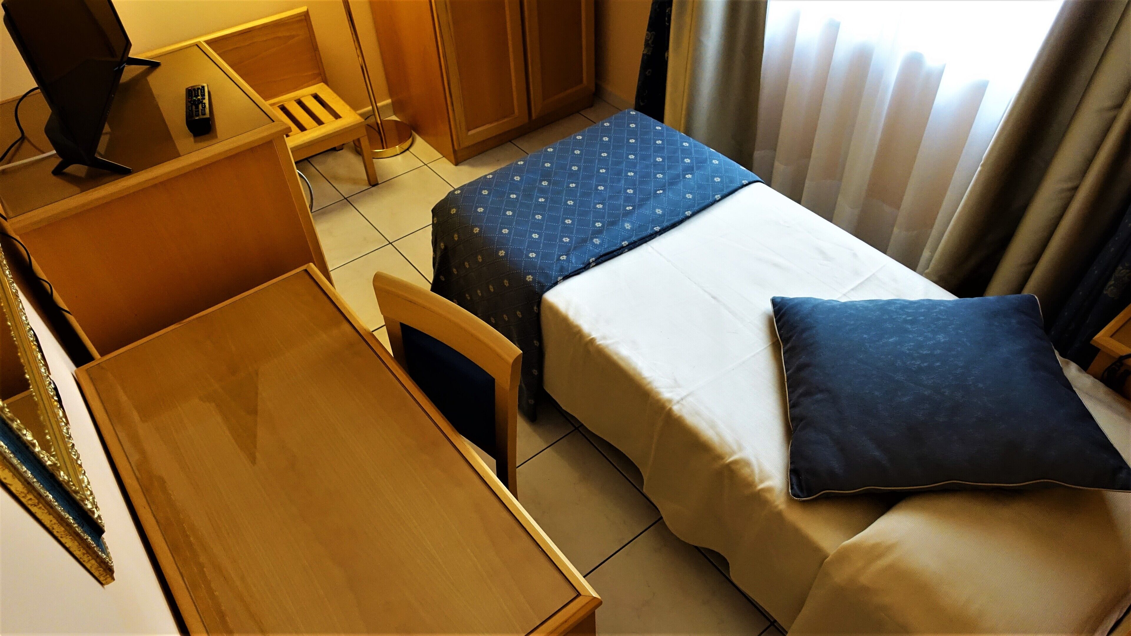 Una camera d'albergo compatta con un letto, una piccola scrivania e una sedia.