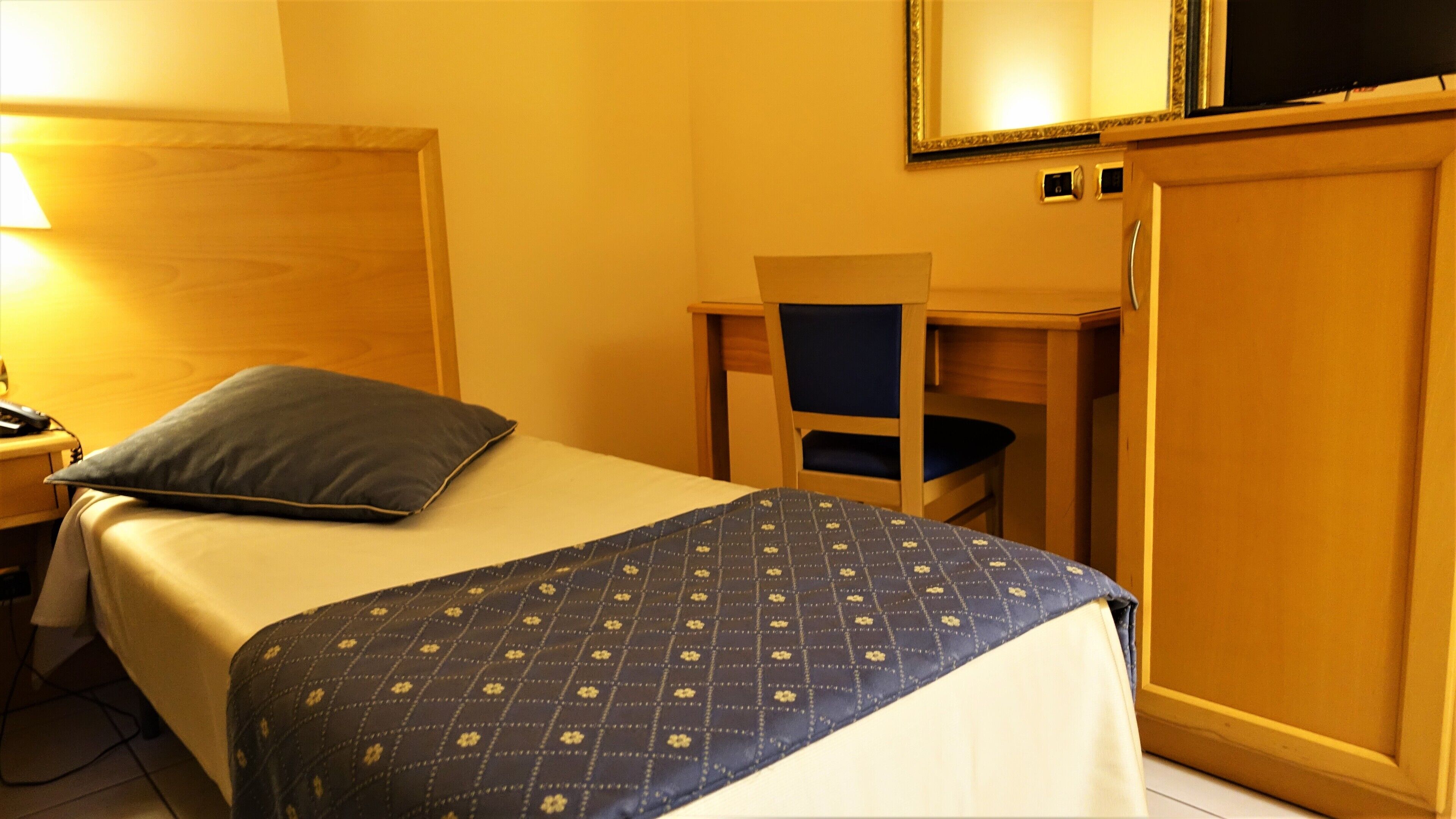 A hotel room with a bed, a desk, a chair, and a wardrobe.