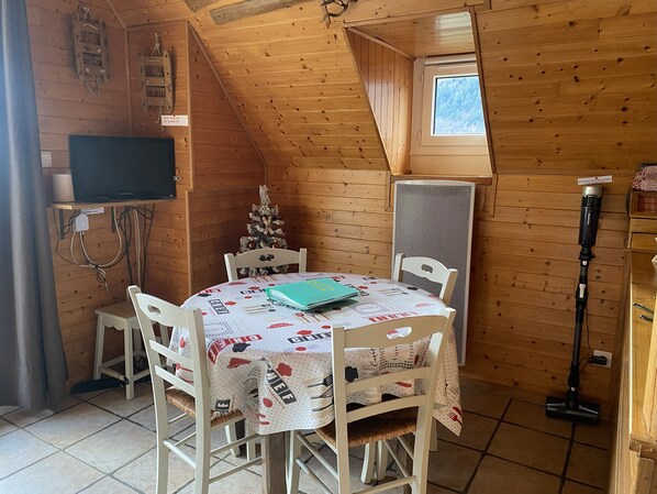 Ett mysigt rum med träinredning, ett runt bord med en festlig duk, ett litet julgran och en tv på en hylla.