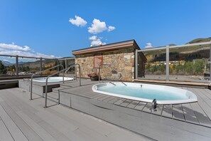 A rooftop deck with two hot tubs, a stone wall, and a view of a mountainous landscape.