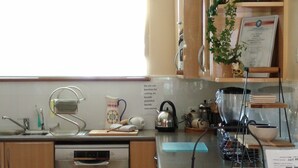 A kitchen with wooden cabinets, a dishwasher, a sink, and a countertop with various items like a kettle, a bowl, and a plant. - ME MATES STUDIO Great stays!! (ESPERANCE)