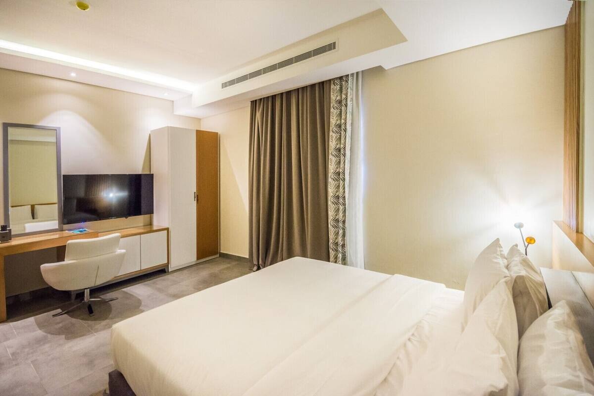 A hotel room with a large bed, a desk with a chair, a TV, and a wardrobe.