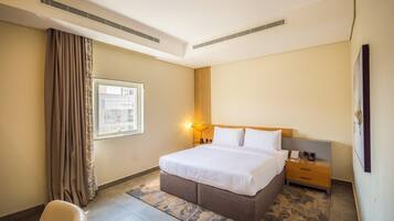 A hotel room with a bed, nightstand, lamp, and a view of the city through the window.