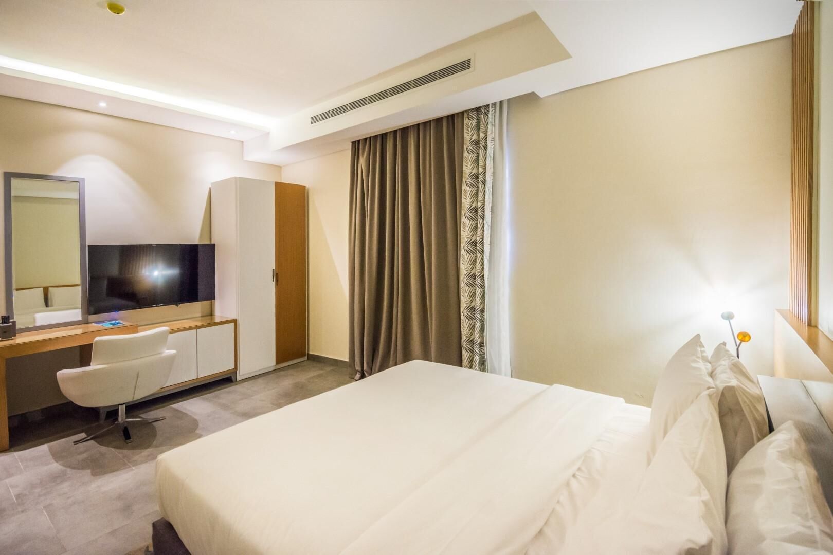 A hotel room with a large bed, a desk with a chair, a television, and a wardrobe.